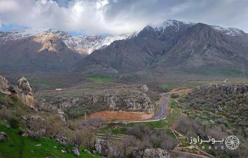 محیط پیرامون غار قوری قلعه کرمانشاه از نمای بالا که فضایی جنگلی و جاده‌ای آسفالته را نشان می‌دهد.